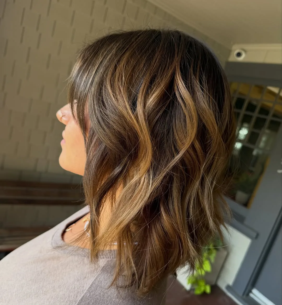 Shoulder-length brunette hair with warm caramel balayage and soft waves, side profile at Salon W
